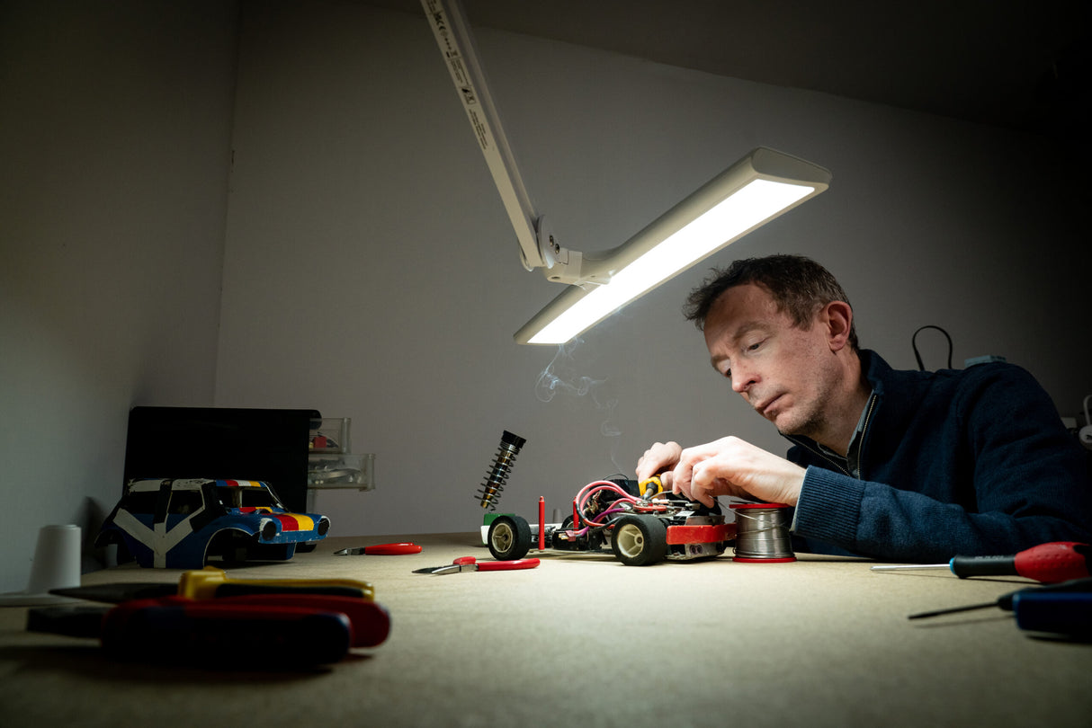 Man soldering a model car under a task lamp