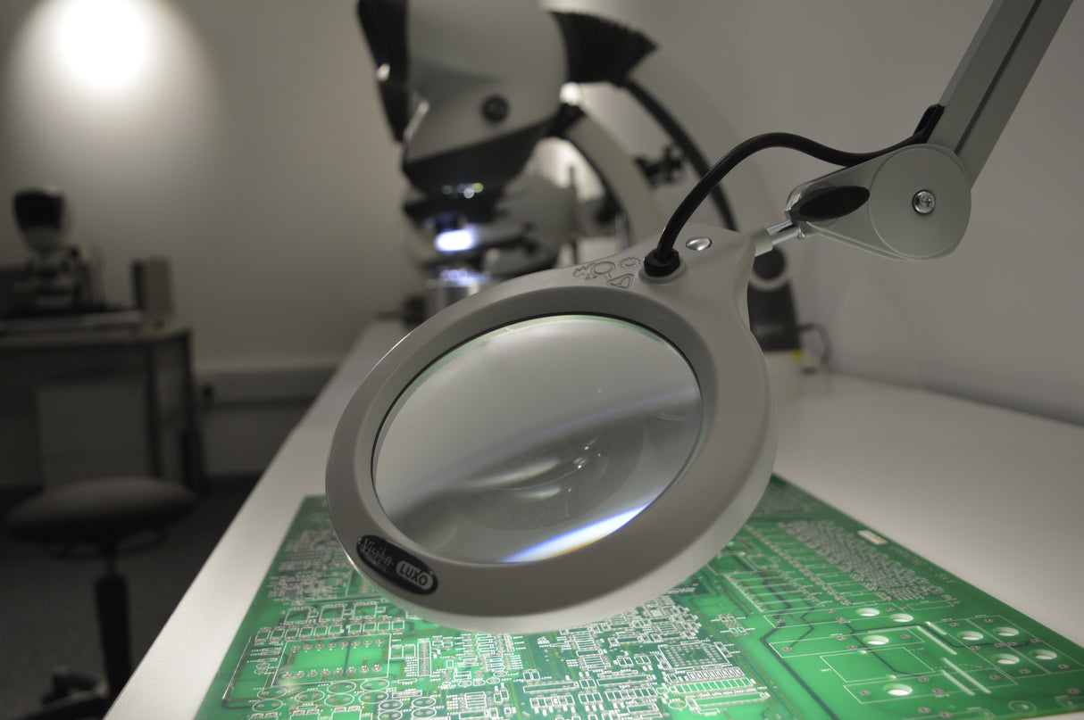 Bench magnifier with PCB underneath on bench in workshop