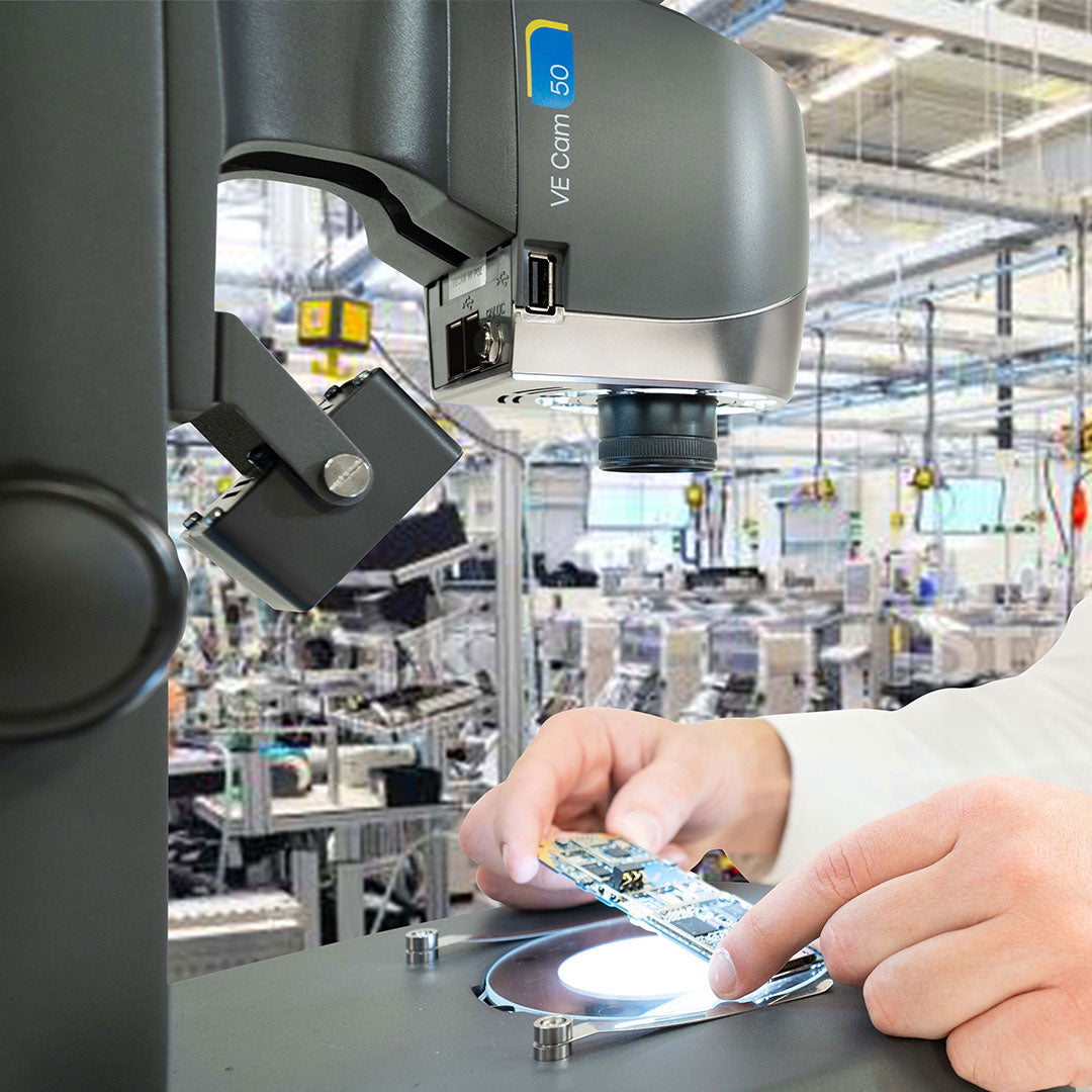 Close up of hands holding electronics circuit board under VE Cam 50 digital microscope in factory